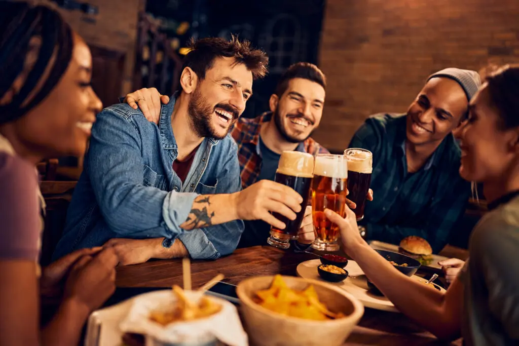 Group of friends cheering their drinks sitting at a table with burgers and fries
