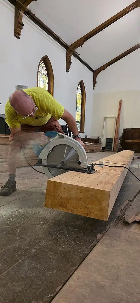 Zach sawing a large wooden beam in the Platz space during renovations